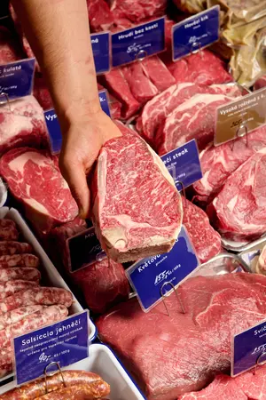 Ruka držící vyzrálý hovězí steak u řeznického pultu.